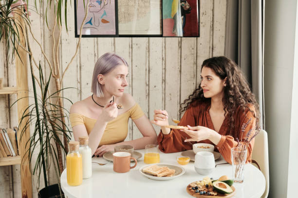 istock Happy young lesbians sitting at dining table and chatting while eating toasts with jam at home 1328757065