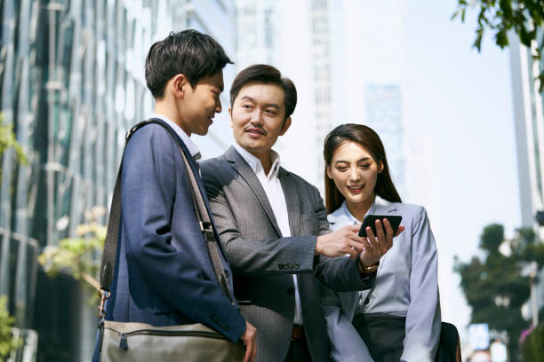 team of three asian corporate executives standing on street discussing business a team of asian business people standing in street having a discussion using cellphone in city downtown shenzhen technology stock pictures, royalty-free photos & images