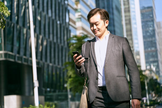 istock asian businessman looking at mobile phone while walking on street 1328777402