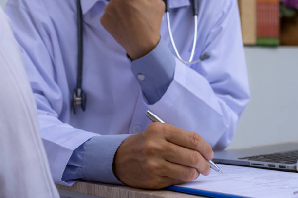 istock Doctor with stethoscope working on laptop computer and writing  note on paperwork in doctor room at clinic or hospital 1328780130