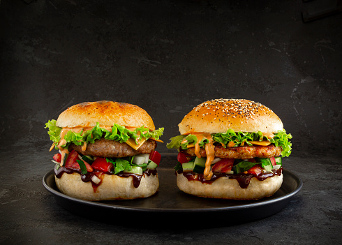 Fresh tasty burgers with chicken and pork on dark background. Fat unhealthy street food.