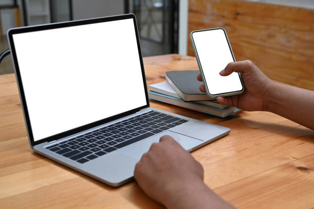 istock Close up view man holding mobile phone and using laptop computer. 1328791428