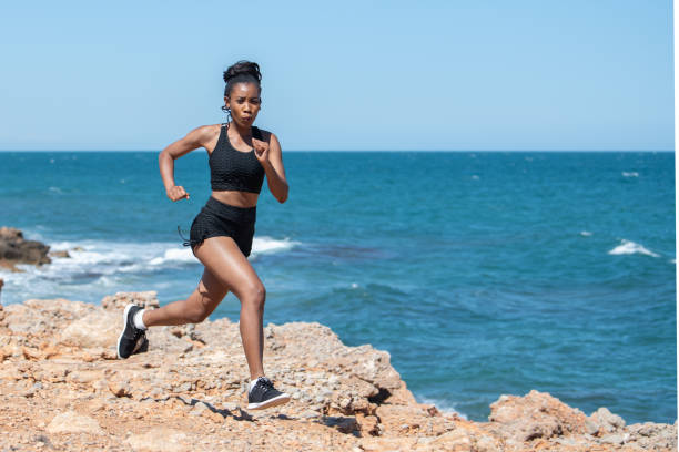 istock Energetic afro american woman running along the coast: Selective focus. Exercise concept 1328797013