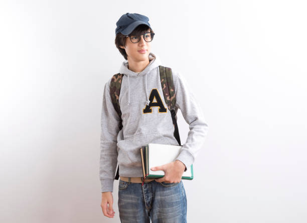 istock Handsome teen boy students carrying a backpack and books standing on white background. 1328797057