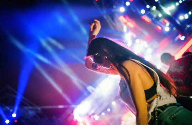 Closeup of a late 20's woman dancing at a rave party. Lasers and spot lights firing in the background over big crowd.