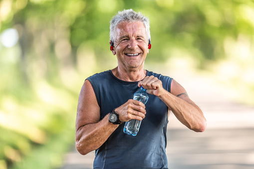 Smiling, fit and retired man with grey hair smiles as he opens up a bottle of water after finishing an aerobic workout.