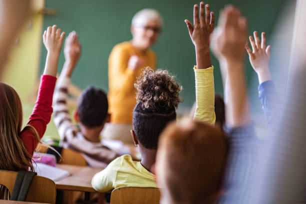 istock Back view of students raising their hands to answer the teacher's question on a class. 1328803274