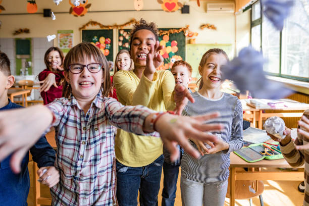 istock Happy school children throwing crumpled papers towards the camera. 1328804194