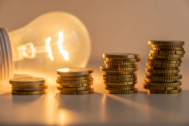 Lit light bulb with coins beside it. Energy tariffs. stock photo