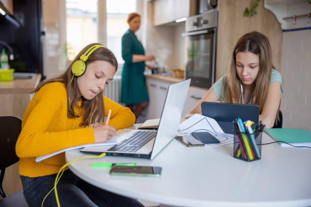 istock Teenage sisters using portable information devices for online learning, mother working at home 1328807893