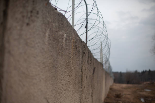 Fence with barbed wire. Fencing around the territory. In the distance, a leaving fence. Concrete wall with wire at the top.