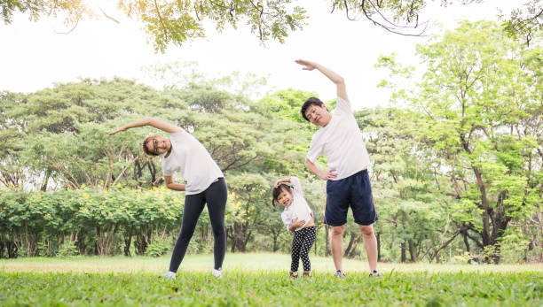 famiglia che si allena e fa jogging insieme al parco. gruppo di famiglia asiatica padre madre e figlia che si allungano dopo lo sport sull'erba. assistenza sanitaria sportiva e concetto medico. - korea child baby asian culture foto e immagini stock