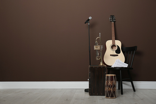 Acoustic guitar, trumpet, hand drum and microphone near brown wall indoors, space for text. Musical instruments