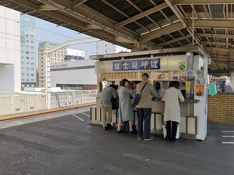 SHIZUOKA, JAPAN - April 7, 2019: People standing eating noodles at a noodle shop at Shizuoka Station, Japan.