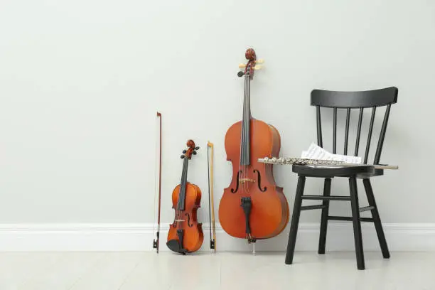 Stringed and wind musical instruments near white wall indoors, space for text