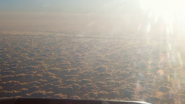 Panoramic aerial view from plane flying above white fluffy clouds at sunrise, sunset