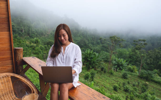istock A woman using and working on laptop computer while sitting on balcony with a beautiful nature view on foggy day 1328814949