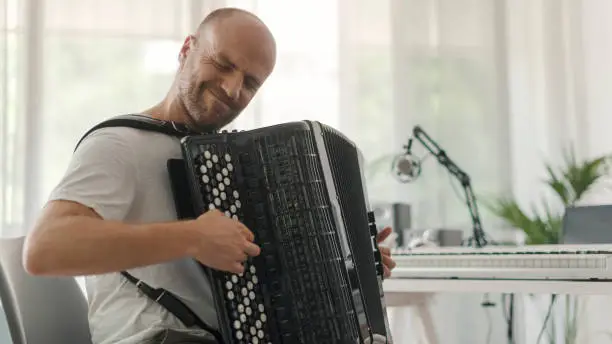 Professional musician sitting in his studio at home and playing the accordion