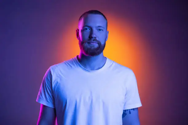 Photo of Close up portrait of young caucasian bearded man isolated on dark studio background in neon lights.