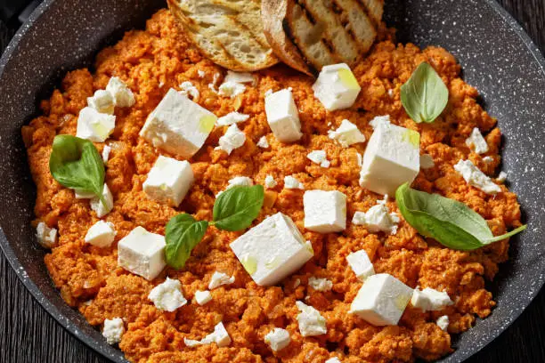 close-up of Strapatsada, eggs scrambled with tomatoes and feta cheese in a skillet with toasted bread, horizontal view, greek cuisine