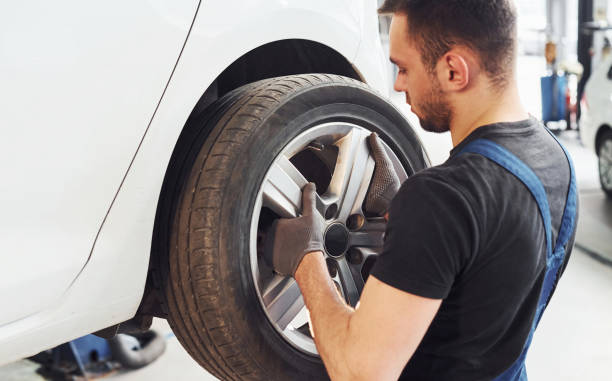 istock Man in work uniform changing car wheel indoors. Conception of automobile service 1328820597