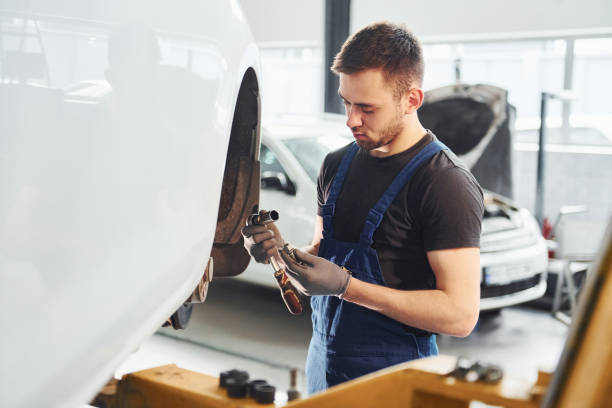 istock Man in work uniform repairs car indoors. Conception of automobile service 1328821002