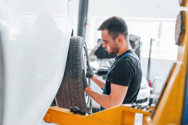 istock Man in work uniform changing car wheel indoors. Conception of automobile service 1328821011