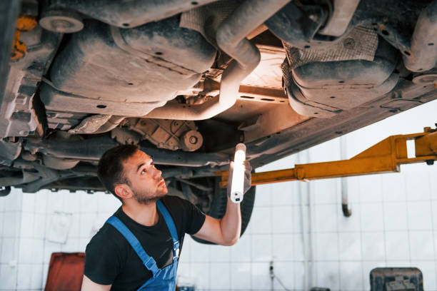 istock Uses lighting equipment. Man in work uniform repairs white automobile indoors. Conception of automobile service 1328821036