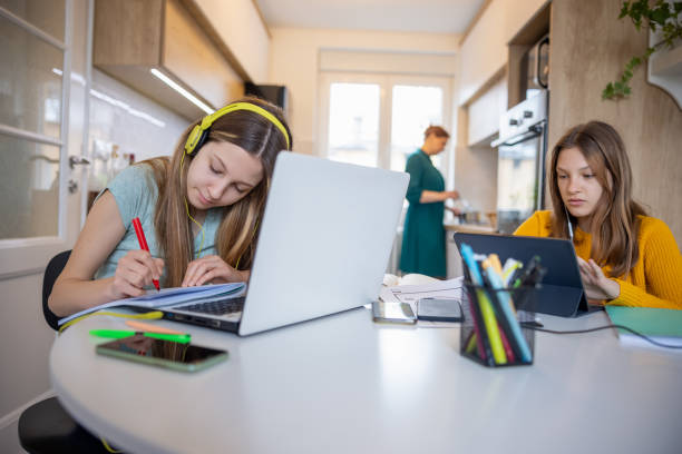 istock Teenage sisters using portable devices for online learning, mother working at home 1328821043