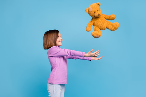 Photo of cute sweet school girl wear purple turtleneck catching brown teddy bear smiling isolated blue color background