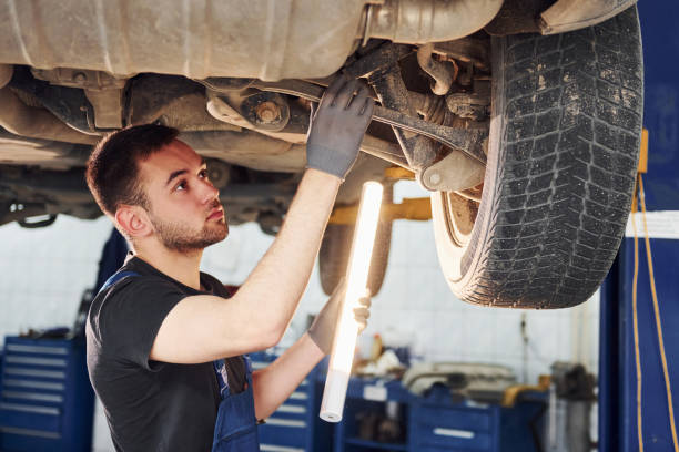 istock Uses lighting equipment. Man in work uniform repairs white automobile indoors. Conception of automobile service 1328822559