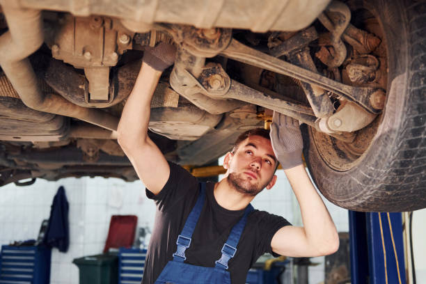istock Man in work uniform standing under car and repairs it indoors. Conception of automobile service 1328822613