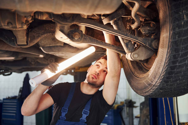 istock Uses lighting equipment. Man in work uniform repairs white automobile indoors. Conception of automobile service 1328822646