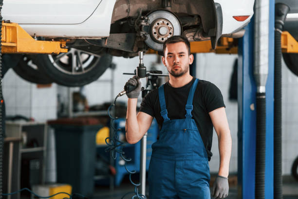 istock Using special tool. Man in work uniform repairs white automobile indoors. Conception of car service 1328822779