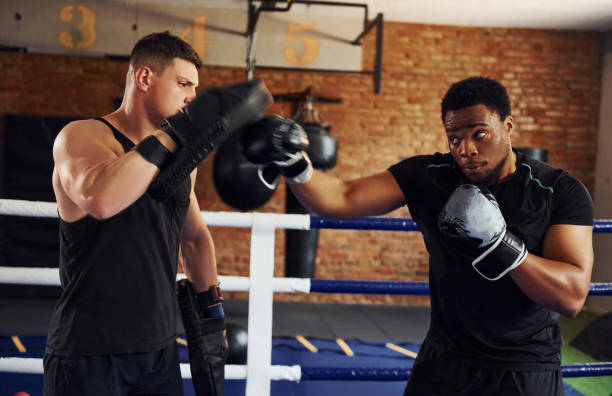 avere il pugilato prattivo. l'uomo afroamericano con ragazzo bianco ha una giornata di allenamento in palestra - boxing winning success challenge foto e immagini stock