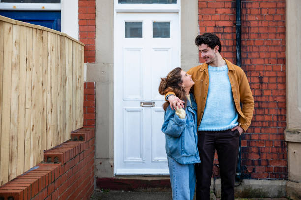 The Next Stage A medium close up view of a young couple stood outside of their new home in Whitley Bay. They are stood affectionately and smiling at each other. northeastern england stock pictures, royalty-free photos & images