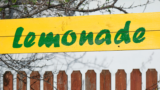 Green Lemonade handwritten text on yellow wooden board sign, next to a fence. Summer fresh drinks, beverage.