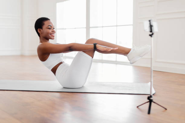 mulher negra sorridente fazendo abdoatos exercício olhando para o telefone - pilates women sit ups yoga - fotografias e filmes do acervo