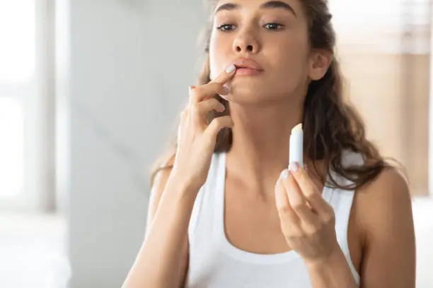 Photo of Young Lady Applying Lip Balm Moisturizing Skin In Bathroom Indoors
