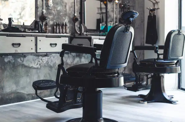 Photo of Two black leather and iron barber chairs in an old style barber shop