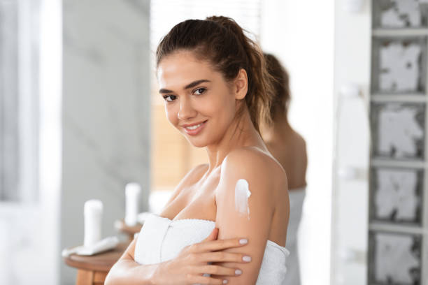 istock Young Lady Applying Cream On Shoulder Moisturizing Skin In Bathroom 1328835241