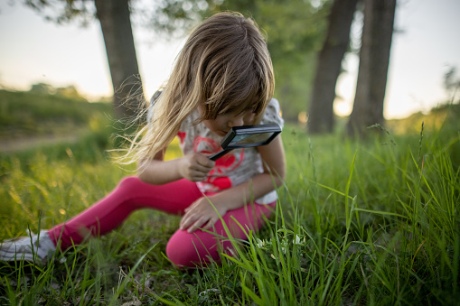 Young girl spending time in nature while looking grass through magnifying glass