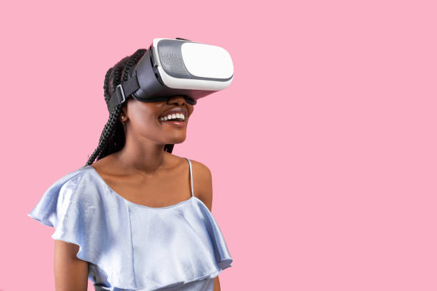 istock Happy young black lady wearing VR headset, exploring cyberspace, using virtual reality on pink background, copy space 1328835528