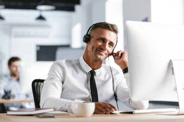 istock Photo of joyful operator man 30s wearing office clothes and headset, smiling while working on computer in call center 1328836684