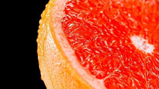 Close-up of water droplets on half of red grapefruit against black background.