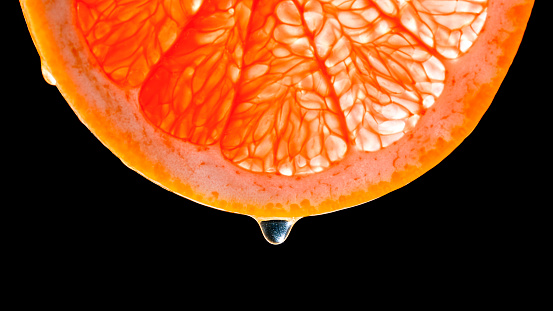 Close-up of drop of water falling off a slice of grapefruit against black background.