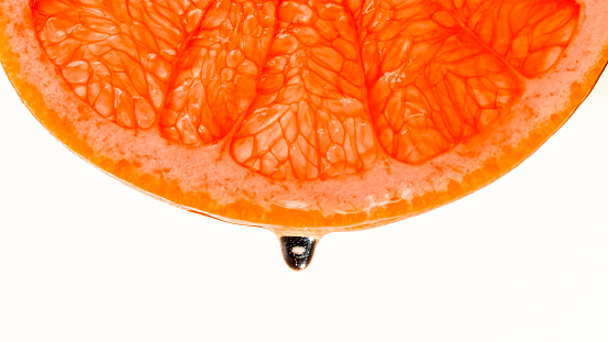 Close-up of drop of water falling off a slice of grapefruit against white background.