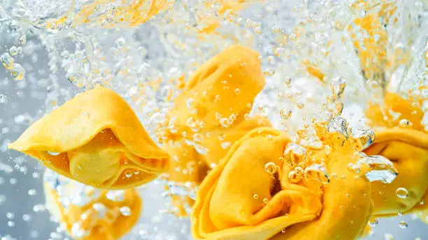 Close-up of tortellini pasta falling into a pot of boiling water.