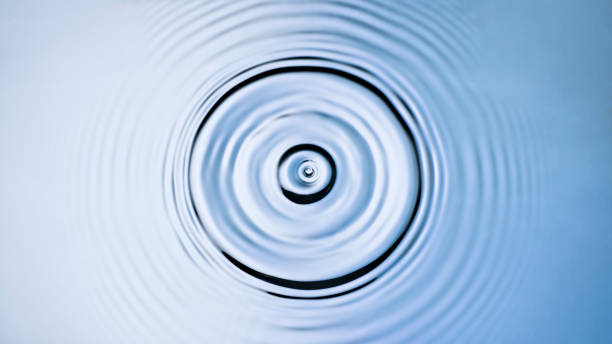 Droplet creating a splash and ripples when hitting the surface Overhead view of droplet creating a splash and ripples when hitting the blue and silver coloured water surface. rippled stock pictures, royalty-free photos & images