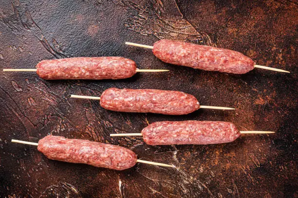 Raw kofta meat kebabs sausages on skewers. Dark background. Top view.